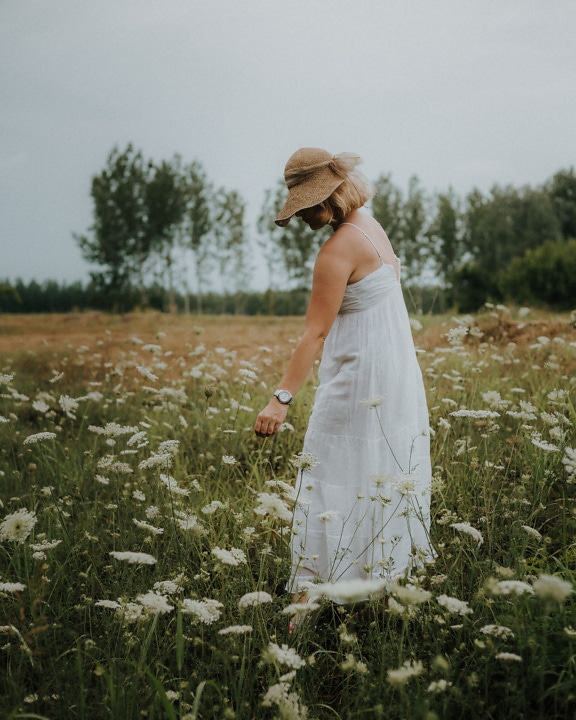 Sombrero de paja anticuado y vestido blanco en modelo de foto en prado