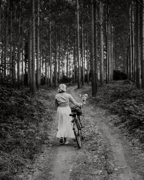 Monochrome photo of woman with bicycle on forest road