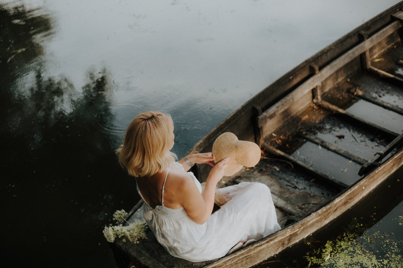Piękna blondynka w sukience i słomkowym kapeluszu w łodzi