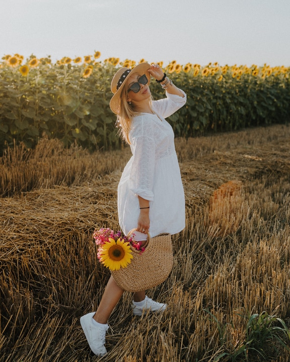 Blondýnka se slaměným kloboukem a proutěným košíkem ve slunečnicích