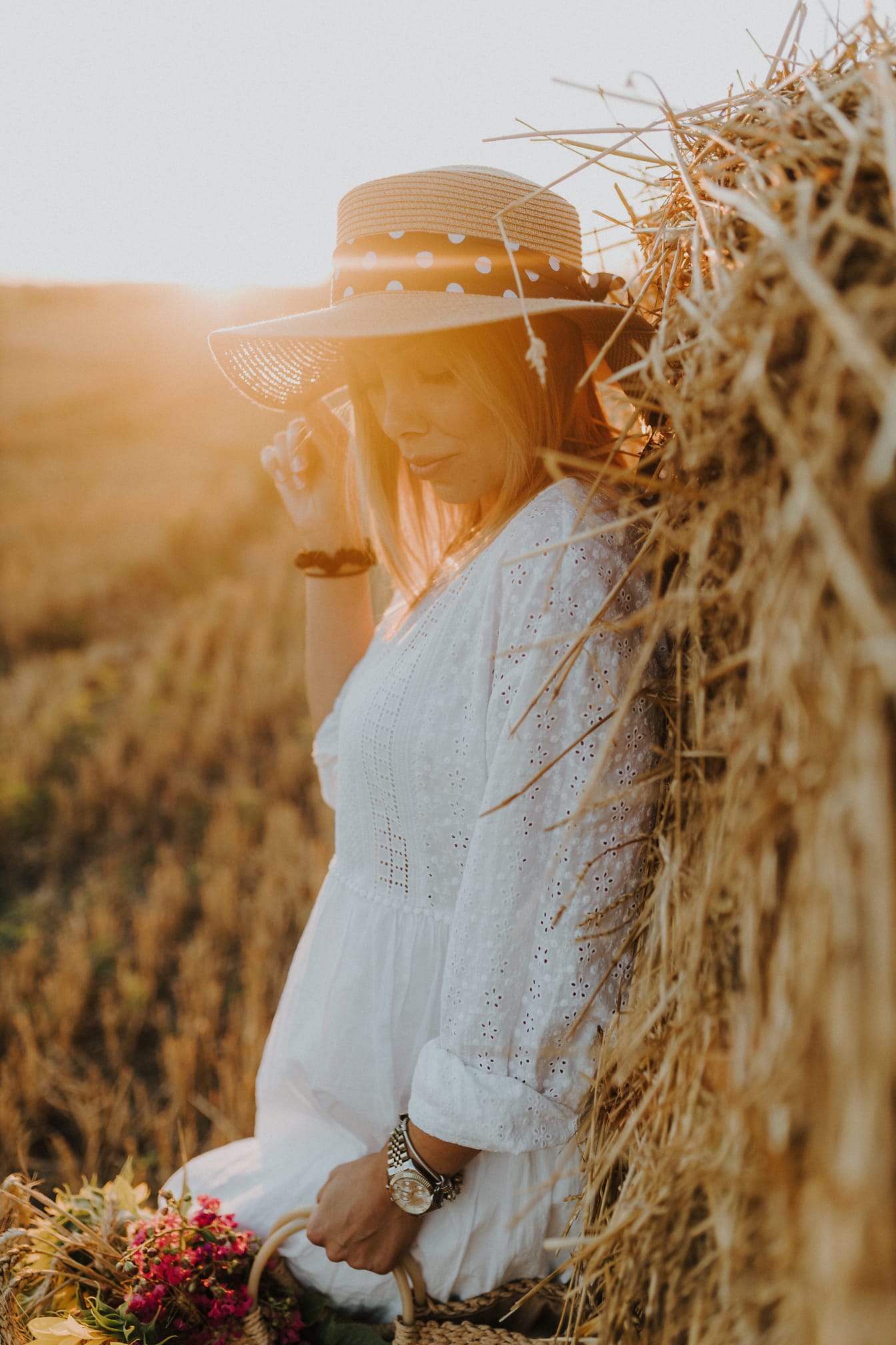 Người phụ nữ trẻ xinh đẹp với chiếc mũ bên đống cỏ khô trên cánh đồng lúa mì