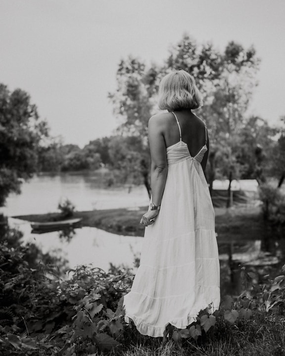 外でエレガントな白いドレスを着てポーズをとる女性のモノクロ写真