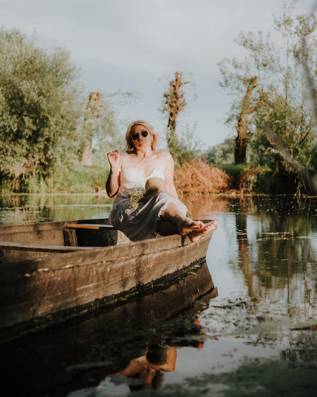 Bionda in posa seduta in barca di legno in riva al lago
