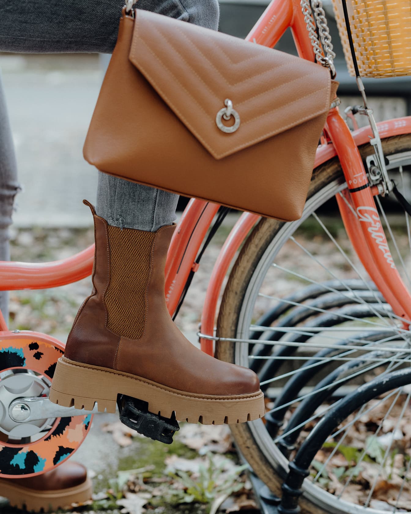 Geantă de mână din piele maro fantezie și cizmă elegantă pe modelul foto pe bicicletă