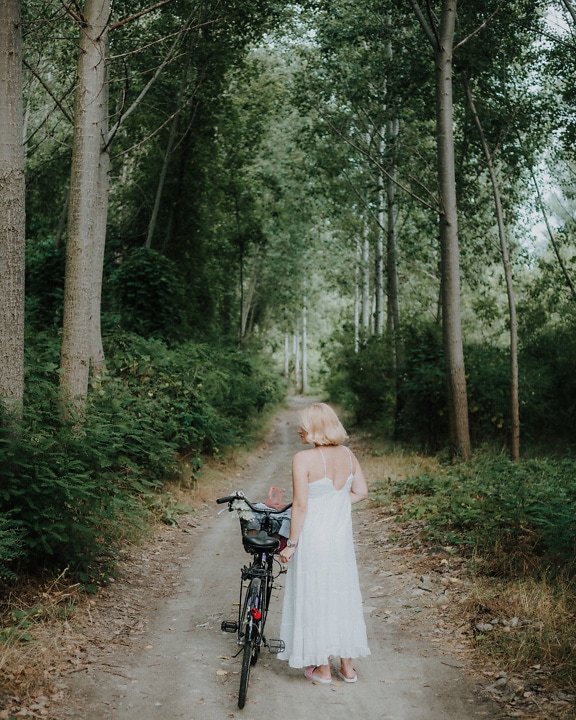 Lady with bicycle on forest trail in green woodland