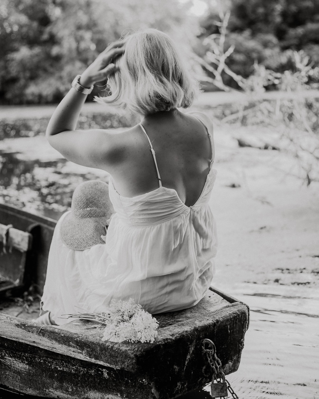 Monochromes Foto einer Dame im weißen Kleid, die in einem Holzboot sitzt