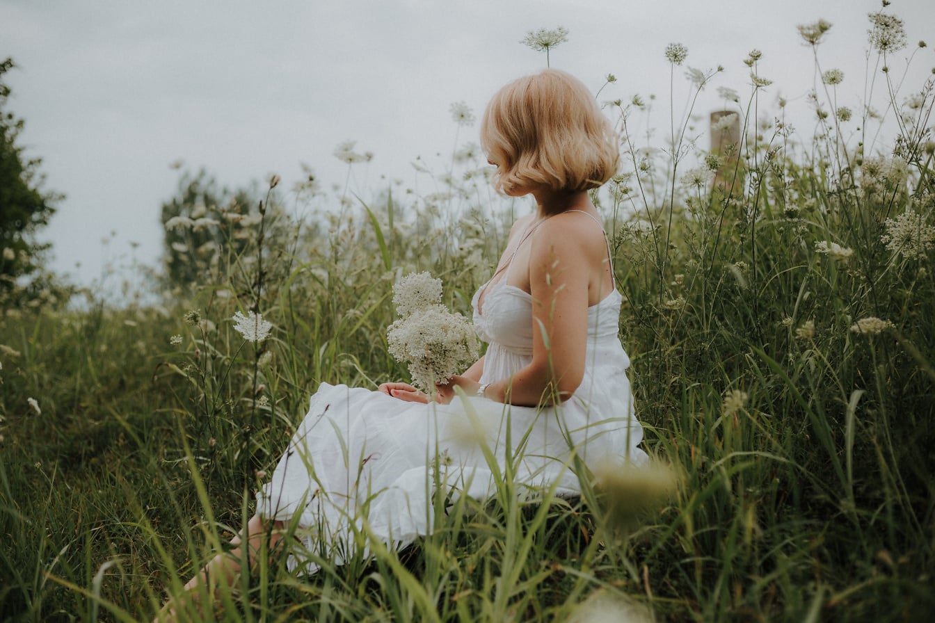 Pirang cantik berpose dalam gaun putih di padang rumput