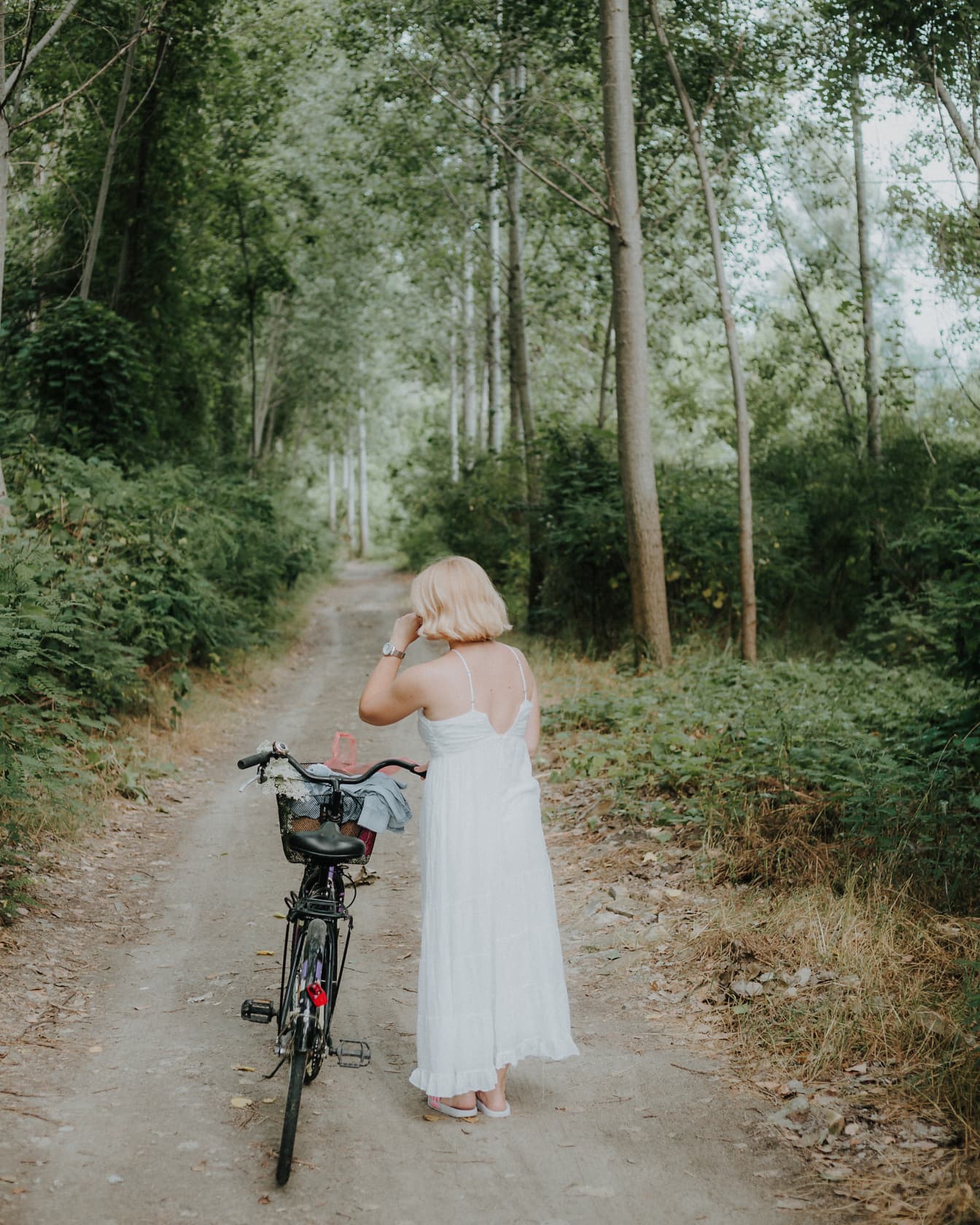 Lässiges weißes Kleid an blonder Frau, die auf Waldstraße spazieren geht