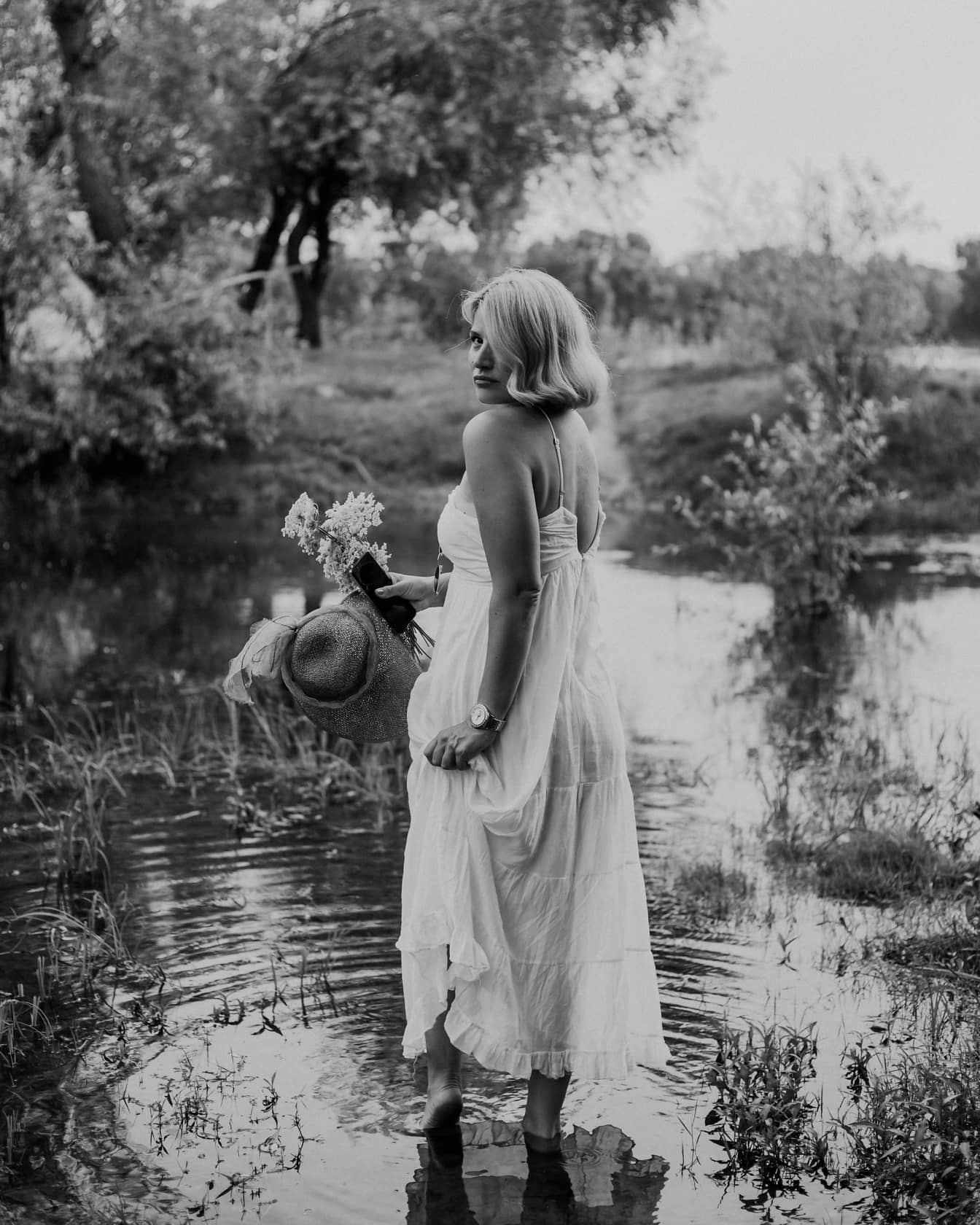 Portret monocrom al blondei desculțe în lac purtând rochie albă