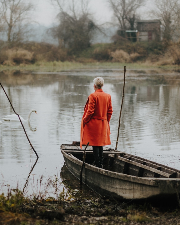 秋のコートを着た木造船に立つ女性