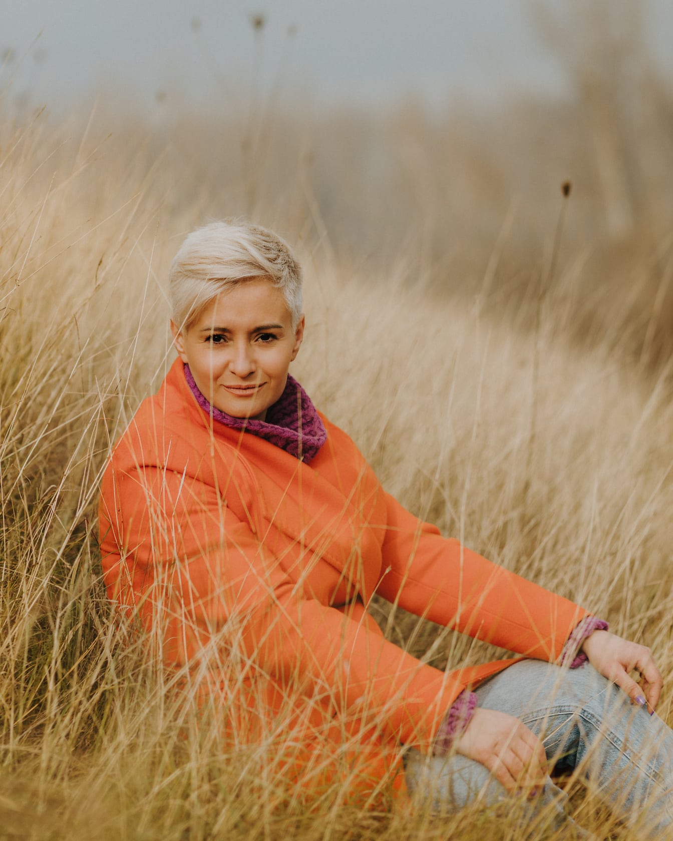 Schönes blondes Fotomodell mit kurzen Haaren sitzt im trockenen Gras