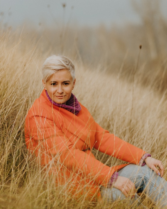 Model frumos de fotografie blondă cu păr scurt, așezat în iarbă uscată