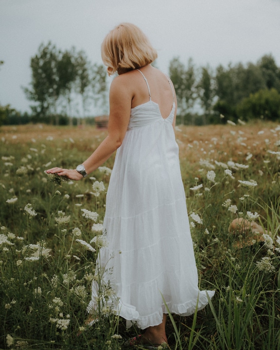 Blonde Frau auf Wiese trägt weißes Kleid