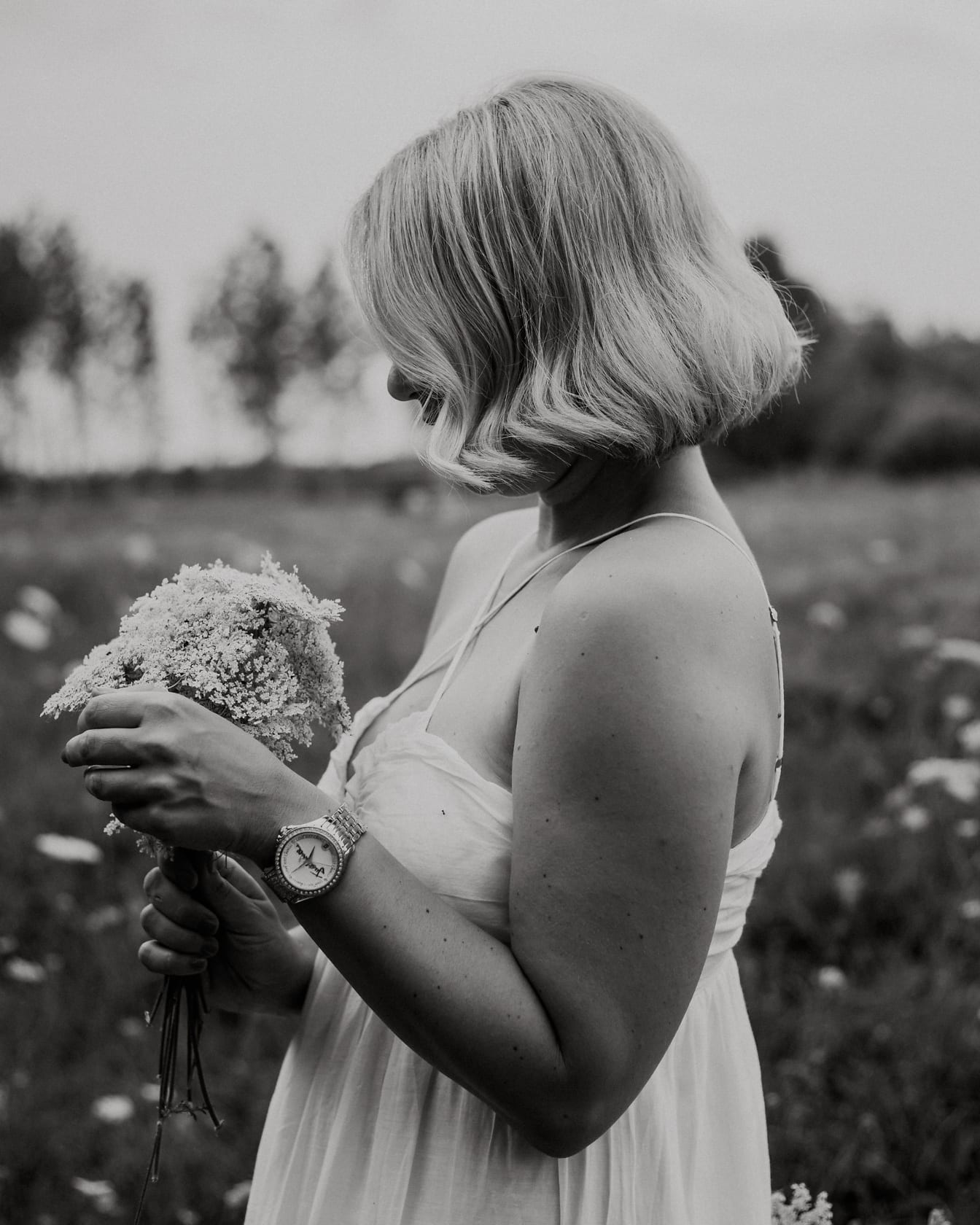 Portrait monochrome d’une femme blonde dans une prairie avec un bouquet
