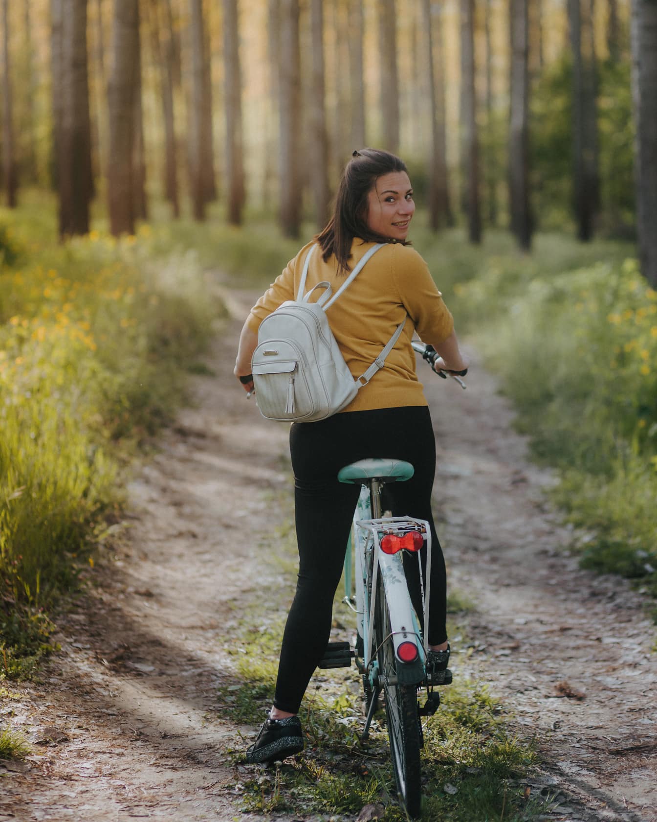 Wesoła brunetka siedzi na rowerze na leśnej drodze i ogląda się za siebie