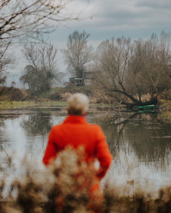 Persoană care stă pe malul râului și se bucură de peisaj în sezonul de toamnă