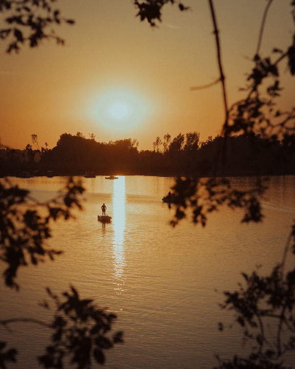Восход солнца с золотым сиянием и силуэтом рыбака в лодке