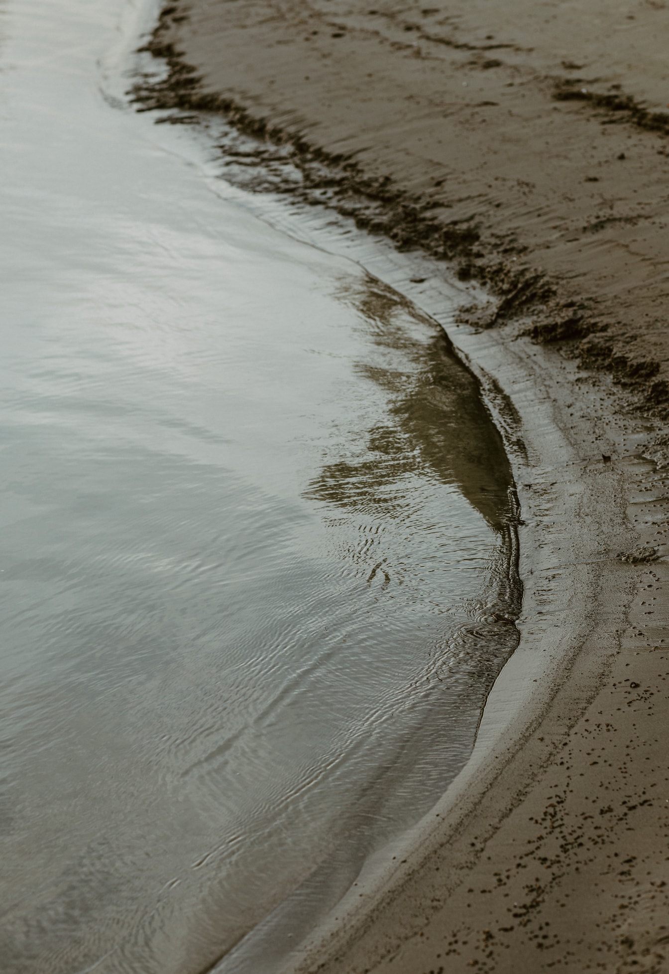Tampilan dekat gundukan pasir basah di tepi pantai dengan ombak