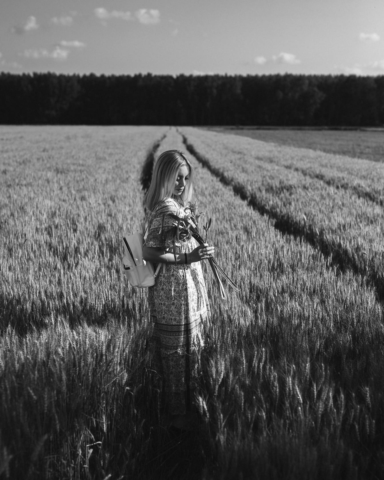 Monochrome photo of woman in wheat field with bouquet of flowers