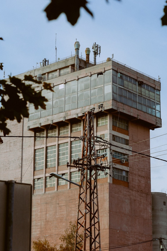 Rusty electric tower in front of building in socialism architectural style