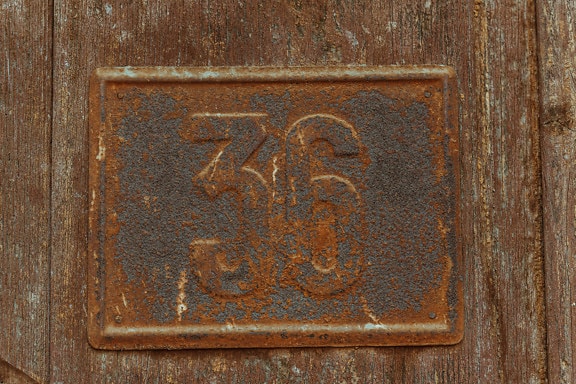 Old metal rusty number on brown plank