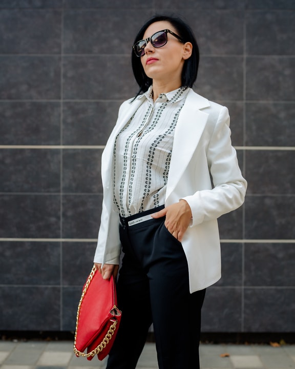Donna d’affari fantasiosa dell’abito di moda con la borsa rossa ed il cappotto bianco