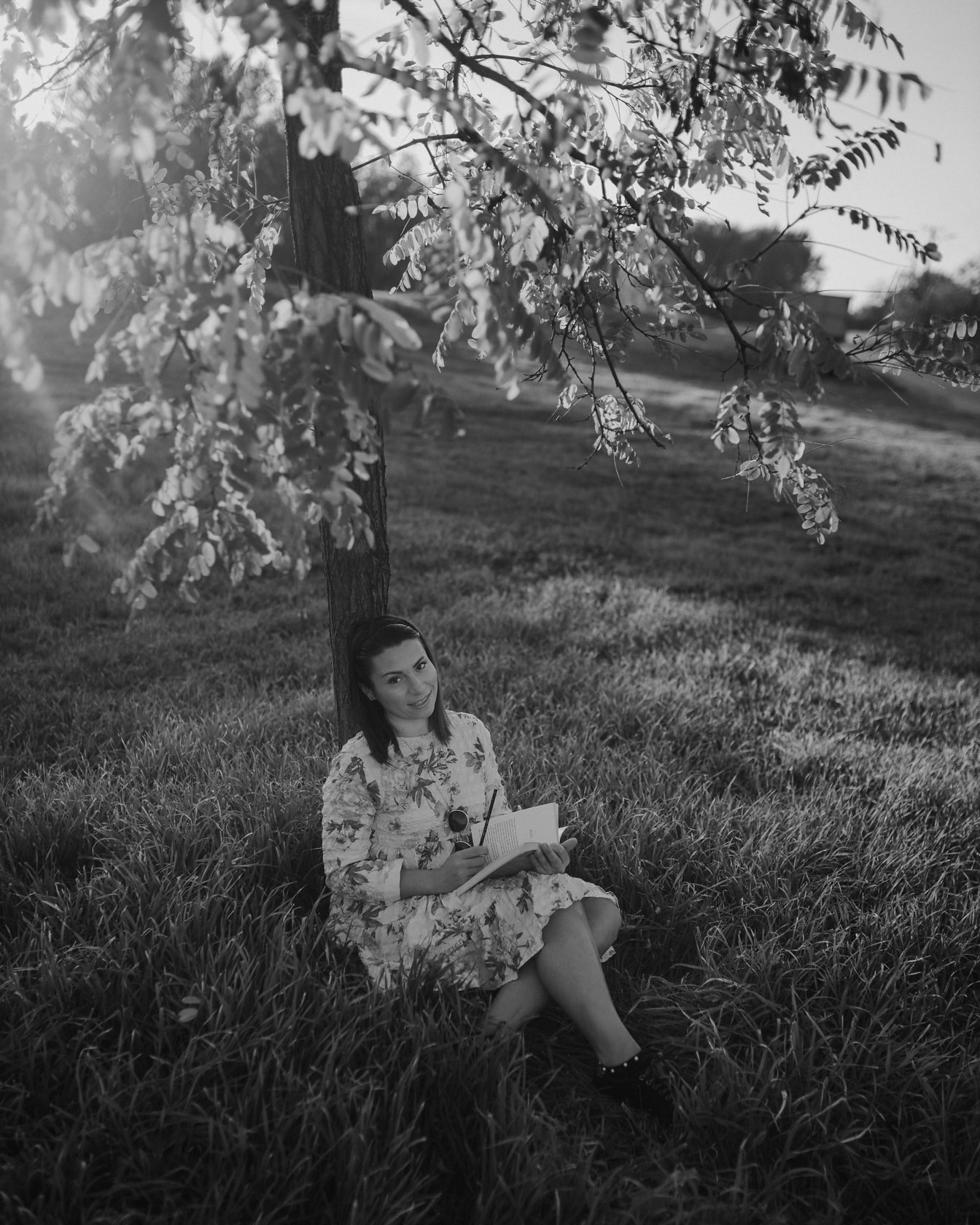 Dievča sedí pod stromom a číta knihu monochromatická fotografia