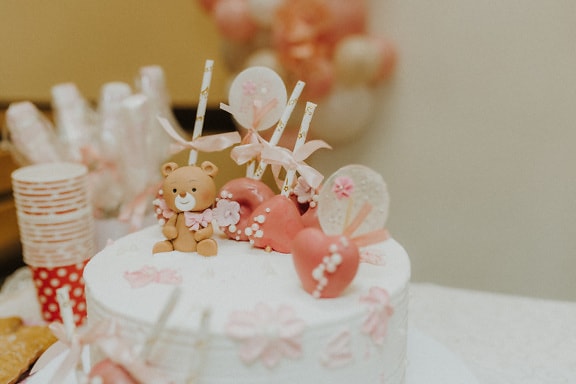 Pastel de cumpleaños con decoración de juguete de osito de peluche y piruletas