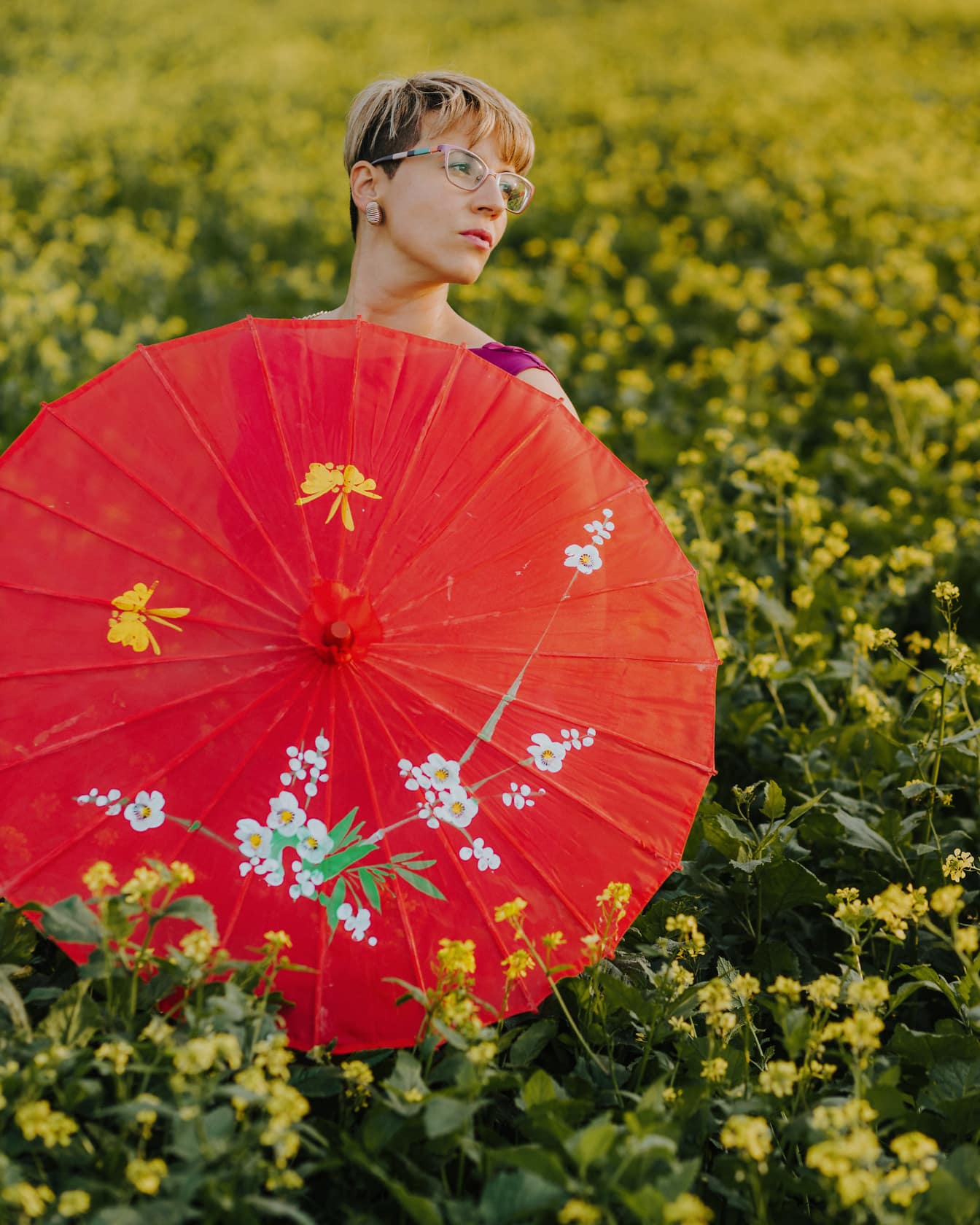 Wanita muda pirang yang menarik dengan payung merah di rapeseed