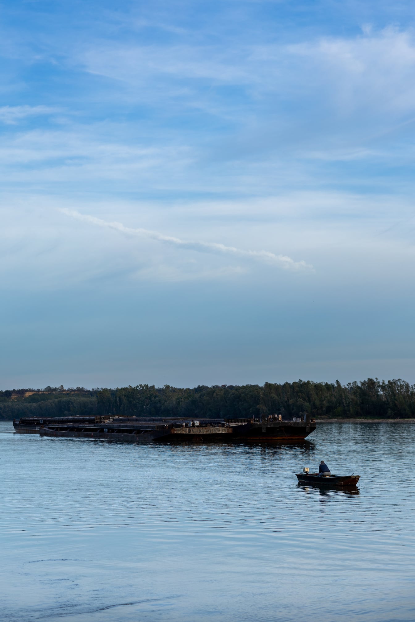Old rusty barge ship on Danube river and small fishing boat