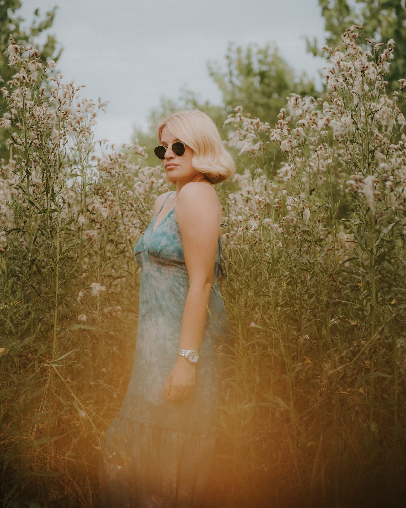 Cô gái tóc vàng quyến rũ trong chiếc váy cotton màu xanh lá cây tạo dáng trên cỏ cao