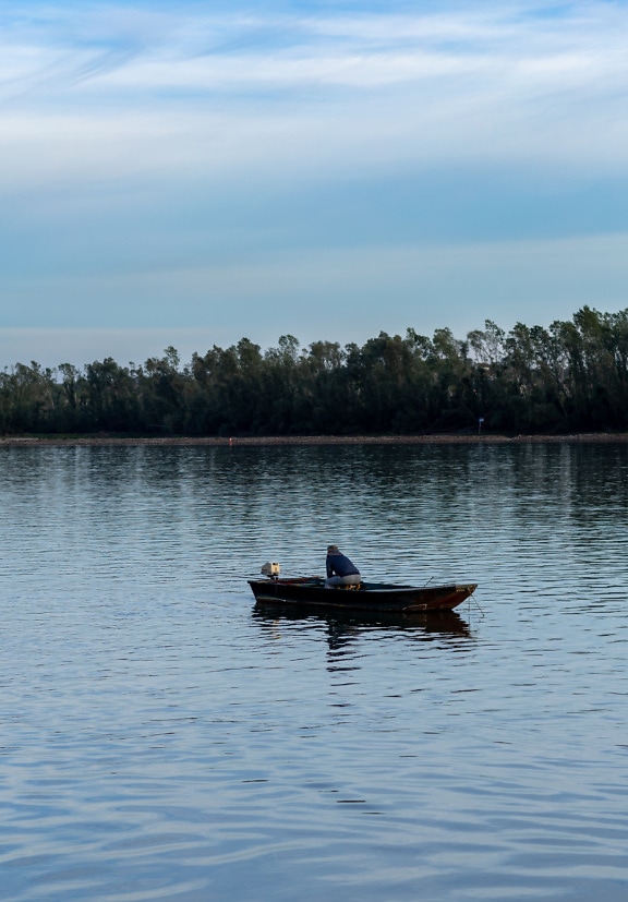 Рибалка сидить в дерев’яному човні і ловить рибу