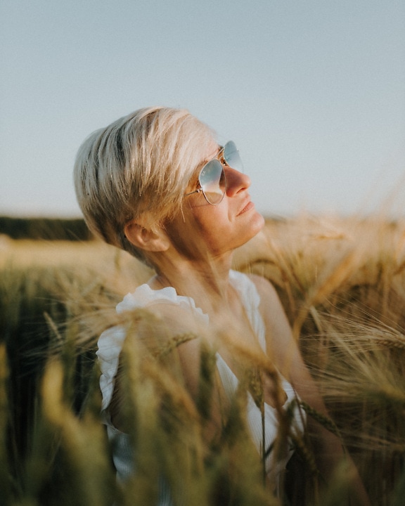 Atraktivní krátké vlasy blond opalující se v pšeničném poli se slunečními brýlemi