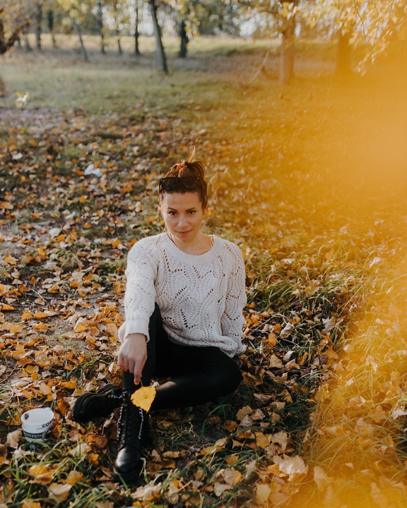 가을 시즌에 햇볕이 잘 드는 공원에 앉아 있는 젊은 여자
