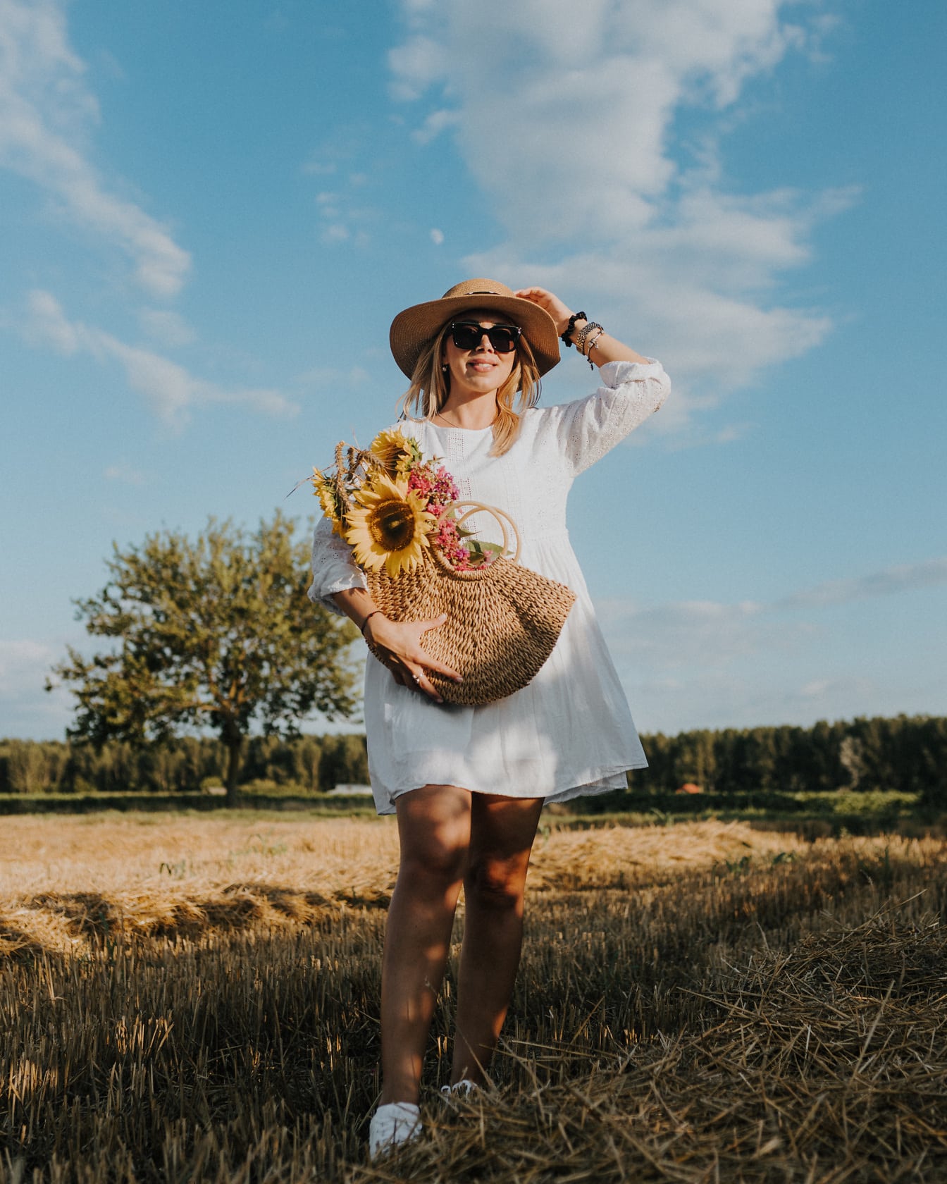 Великолепная фотомодель с плетеной корзиной и соломенной шляпой на пшеничном поле