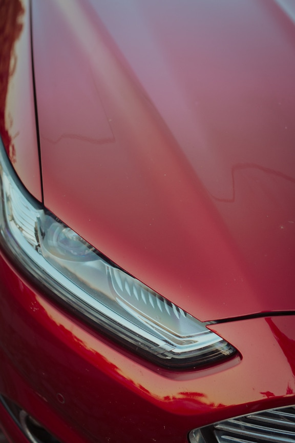 Close-up of headlight of dark red metallic sports car