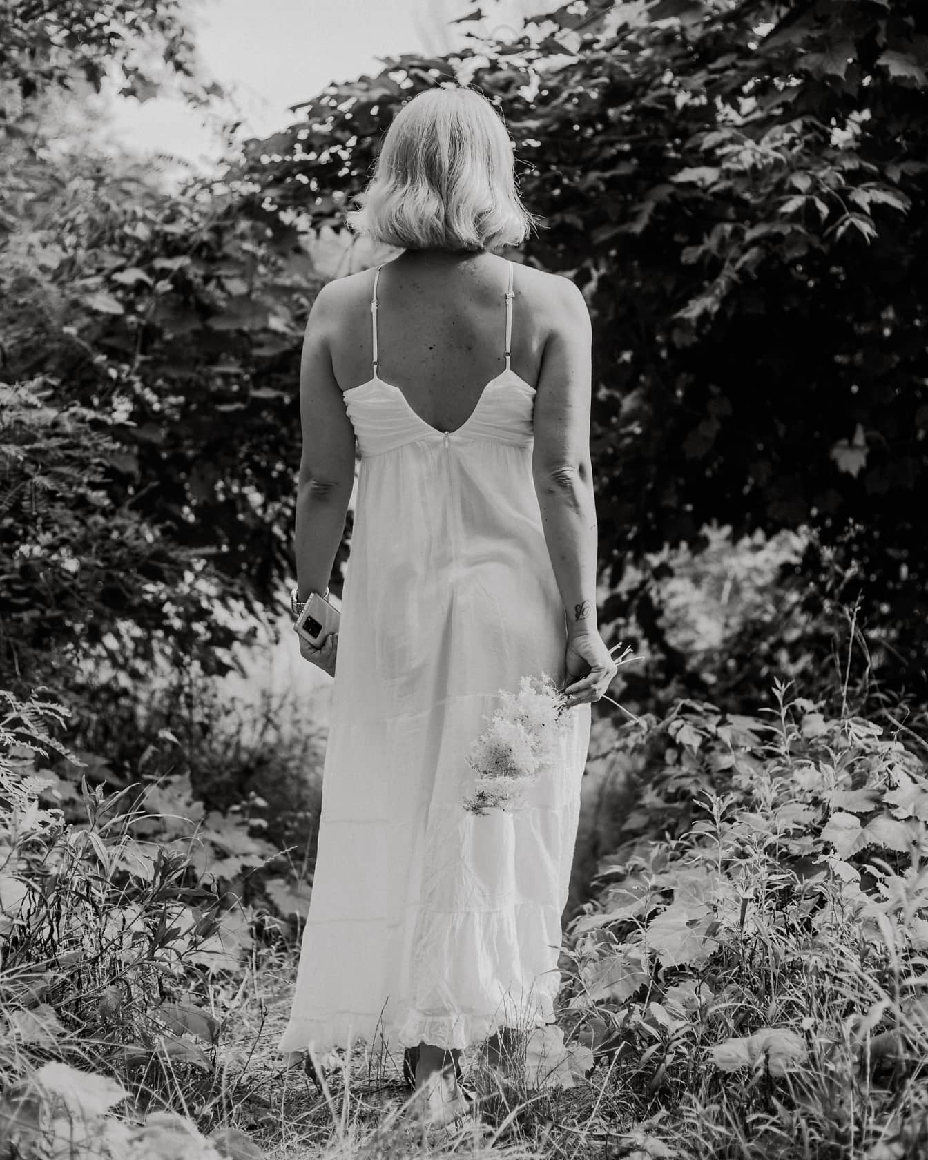 Svartvitt foto av ung kvinna i vit klänning i buskar