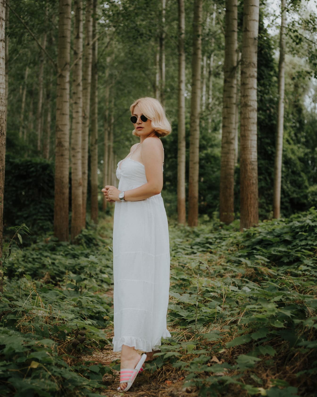 Великолепная блондинка в белом платье в зеленом лесу