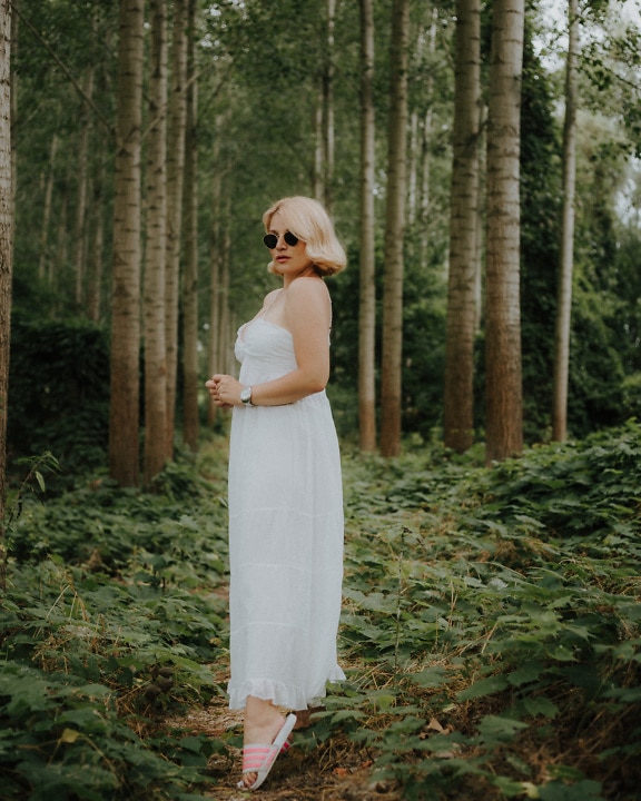 Hermosa rubia en vestido blanco en bosque verde