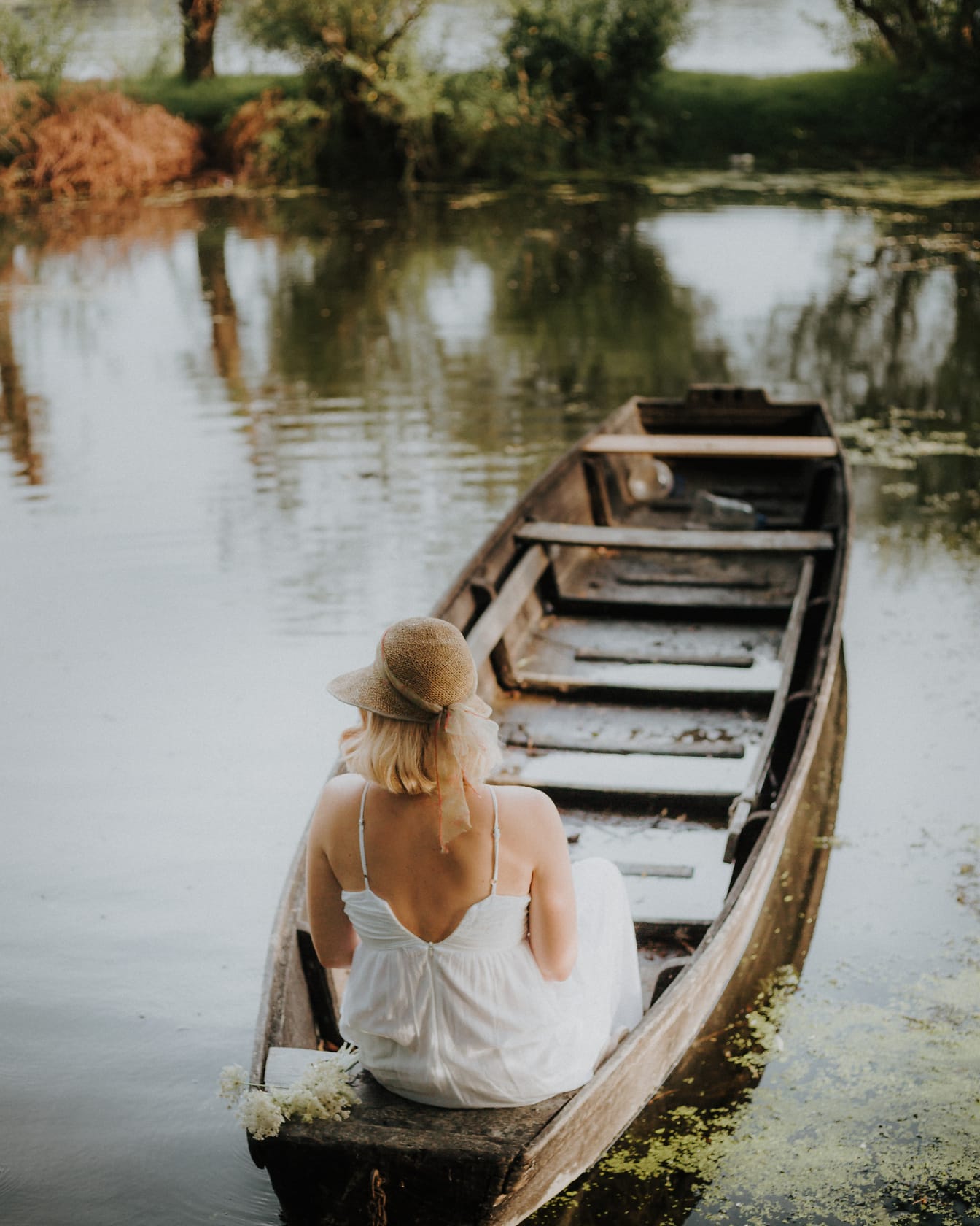 Fotomodel poserer i båd med stråvarme og gammeldags kjole