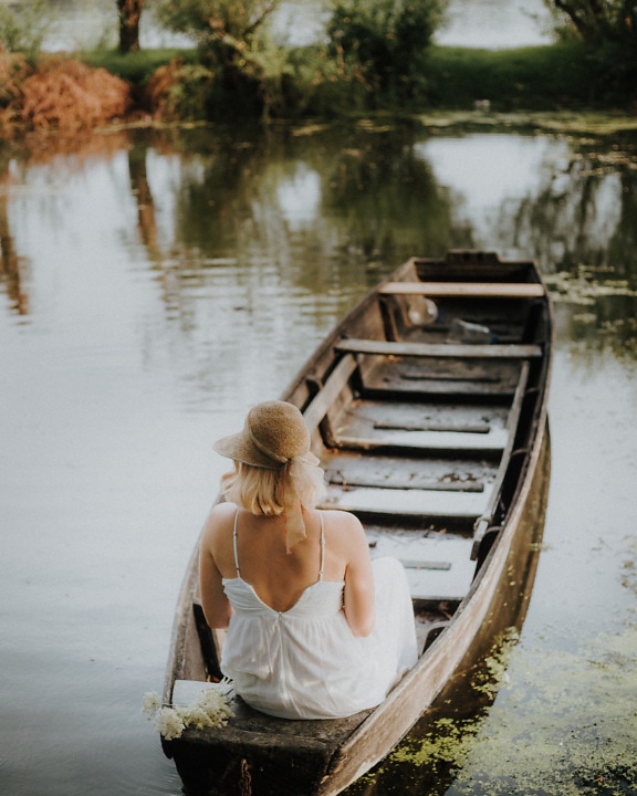 Model foto pozând în barcă cu căldură de paie și rochie de modă veche