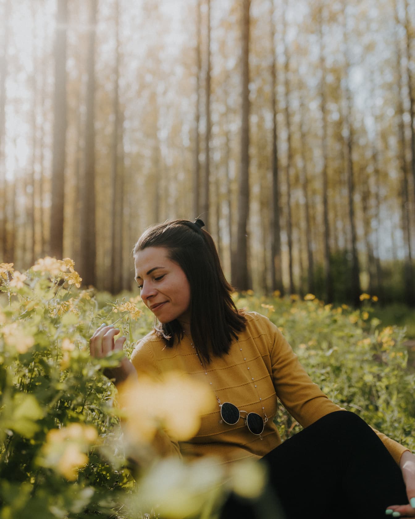 Iloinen hyvännäköinen ruskeaverikkö istuu kukissa metsässä