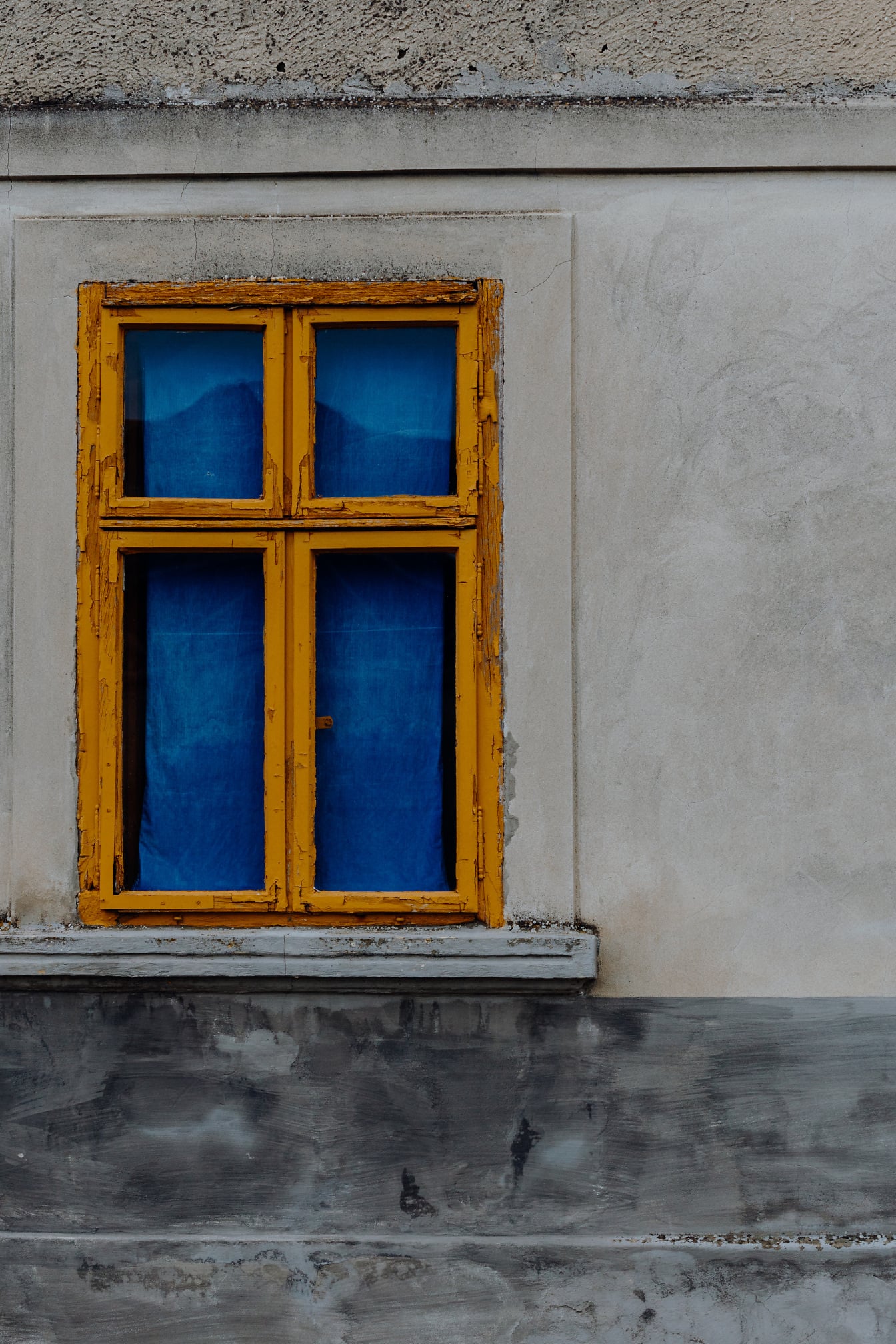 Żywa żółtawo-brązowa farba na starym oknie z ciemnoniebieską zasłoną
