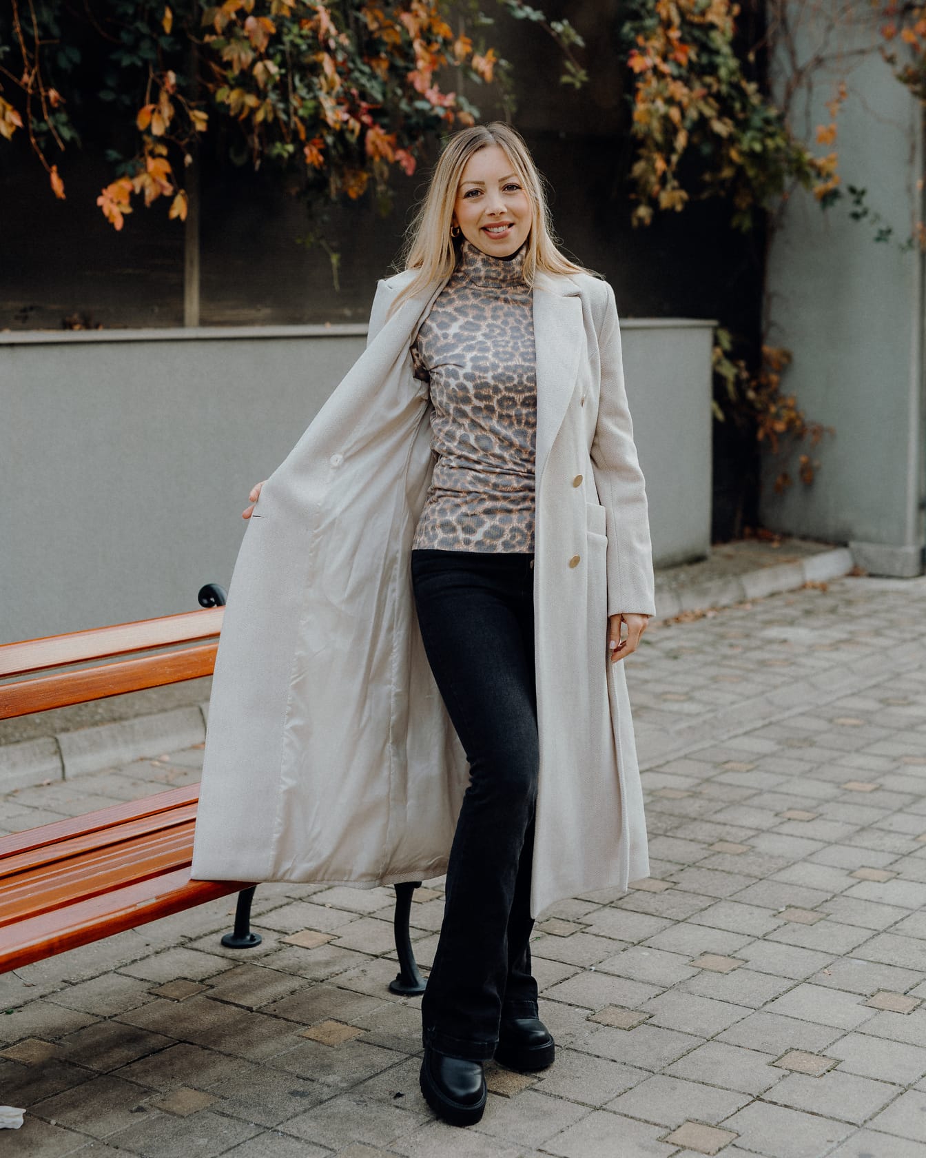 Blonde posing in beige coat and black pants and boots