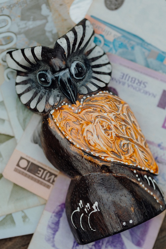 Burung hantu kayu buatan tangan kepala hitam dan putih dan uang kertas sebagai latar belakang
