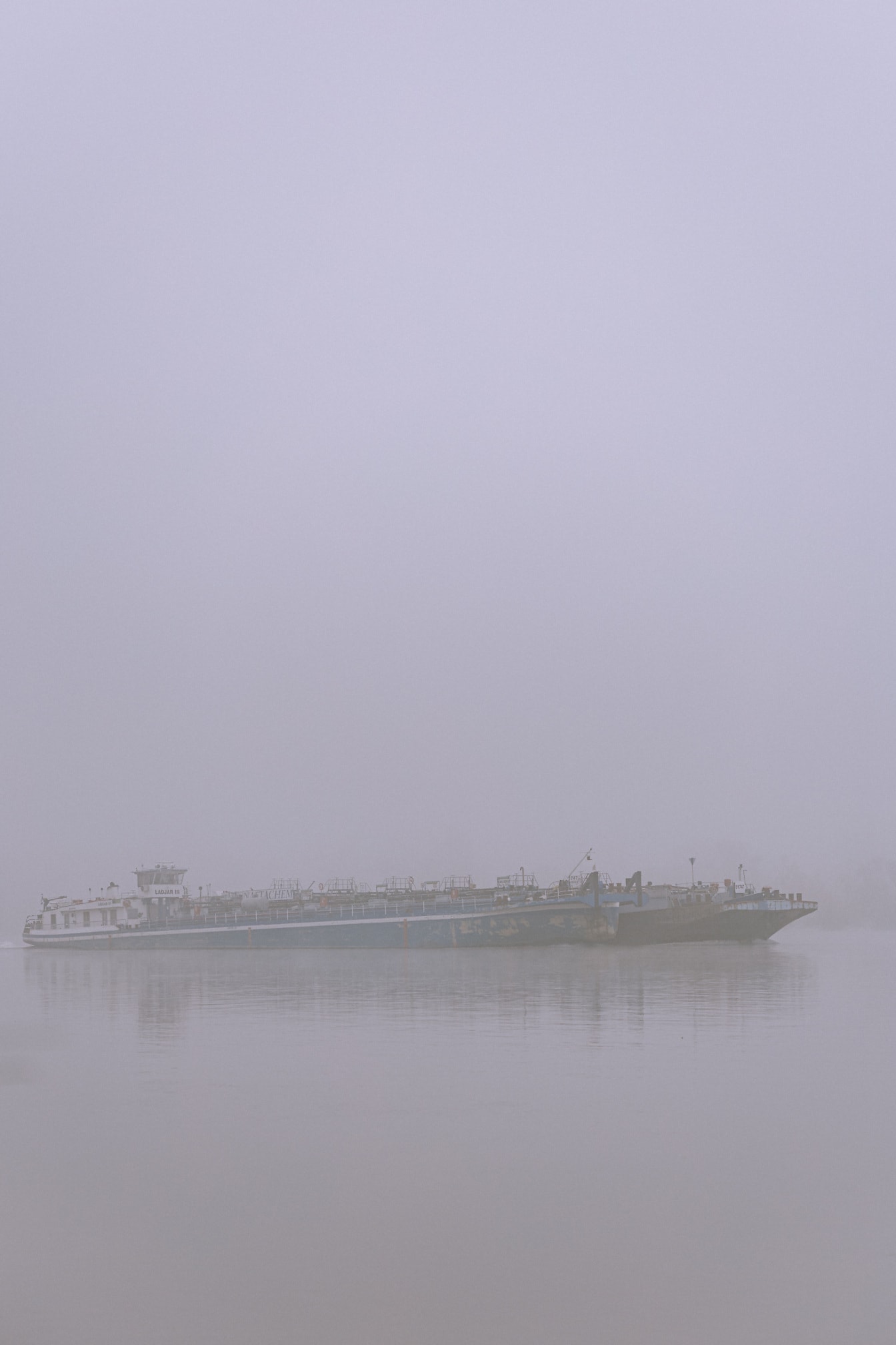 Kontur av pråmlastfartyg i dimma på floden