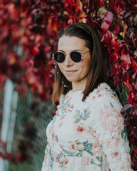 Portrait of attractive brunette with round sunglasses with reddish ivy background