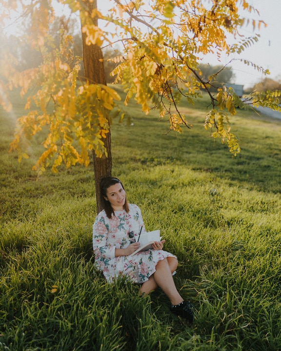 Hermosa mujer joven sentada en el prado y leyendo un libro en un día soleado