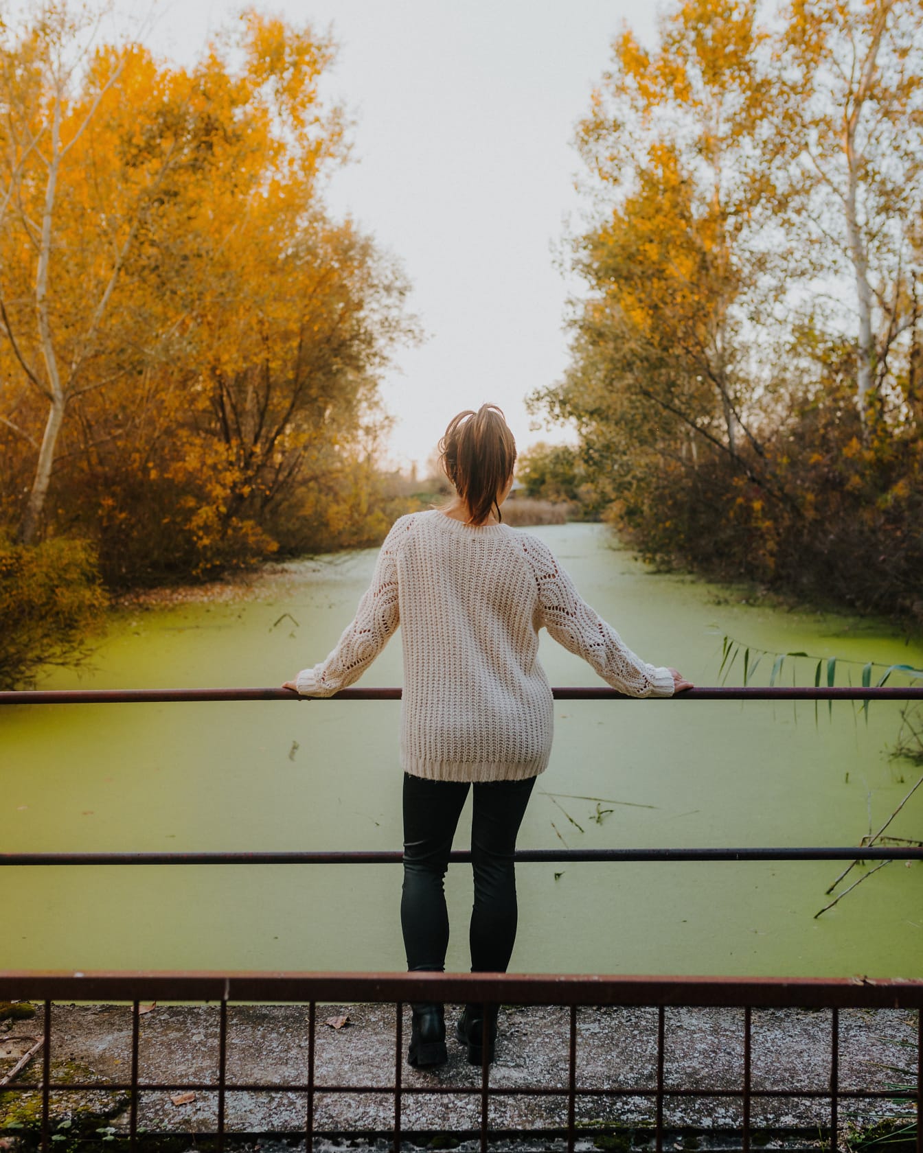 Mulher no suéter de lã na ponte de pedestres sobre o canal