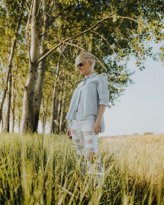 Woman in casual white trousers and blue shirt in countryside on sunny day